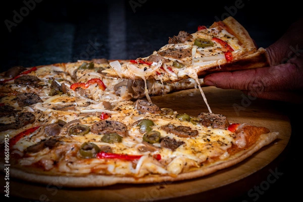 Obraz Close-up of a hand taking a slice of vegetarian pizza with onions, bell pepper, and vegetables on a wooden board.