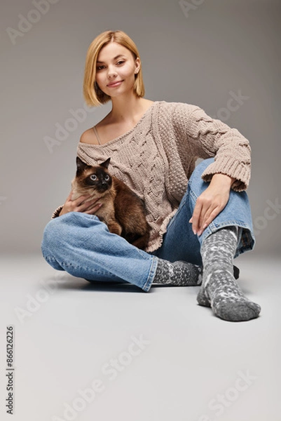 Obraz A woman with short hair seated on the floor, lovingly holding her cat while sharing a moment of connection at home.