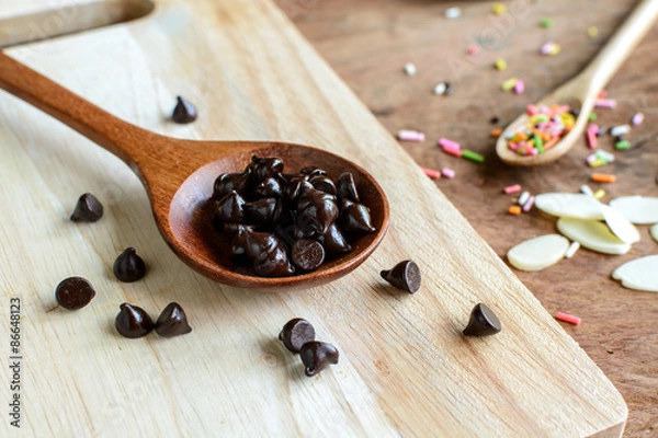Fototapeta Chocolate chips on wooden spoon and ingredients for cooking