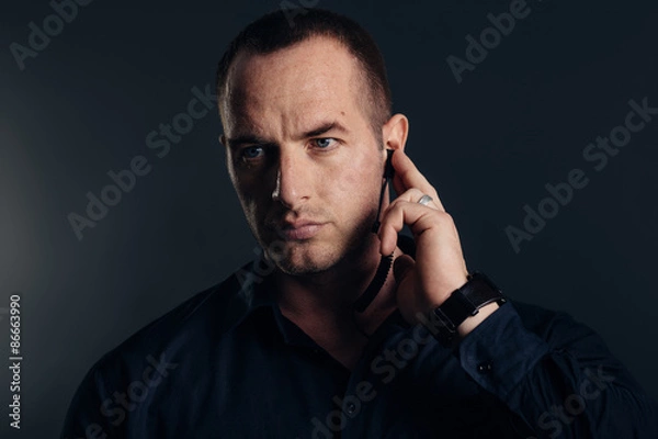 Obraz Security detail, bodyguard holding earpiece. Studio shot.