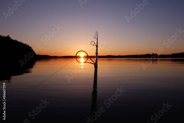 Fototapeta Sunset on a lake in Finland seen through a fishing rod ring on a warm and serene summer evening
