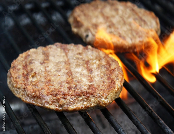 Obraz Juicy beef burgers sizzling over hot flames on the barbecue
