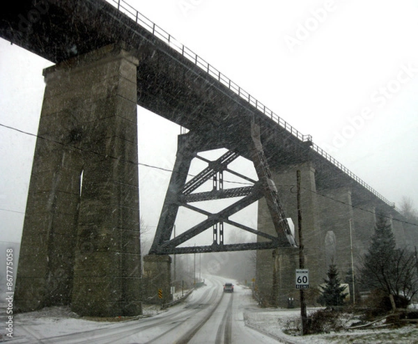 Obraz Driving under an old railway trestle bridge during a snowstorm.