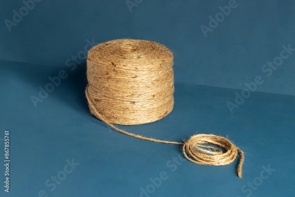 Fototapeta Close-up of a large spool of natural jute twine against a blue background, ideal for crafting, packaging, and gardening projects.