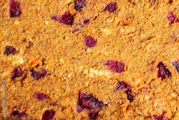 Fototapeta Close-up of a textured baked food surface with visible chunks of dried plums and other ingredients. The golden-brown crust showcases a delicious blend of natural ingredients. Organic texture.