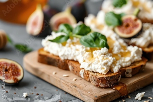 Fototapeta Delicious bread toasts topped with ricotta cheese, figs, honey, and fresh basil leaves on a wooden board. Perfect gourmet breakfast.