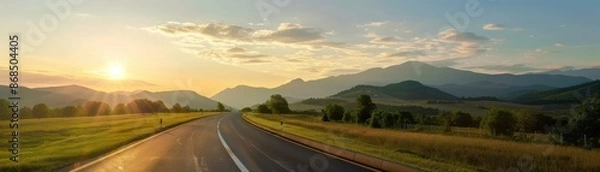 Fototapeta A scenic road extending into the horizon during a peaceful sunrise, surrounded by lush greenery and distant mountains.