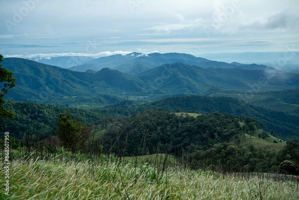 Fototapeta Lush green mountains with a cloudy summer sky stretch into the distance