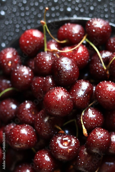 Fototapeta Cherry berries on a black background, close-up. Wet sweet ripe cherries. Dark red cherries with green stems covered with fine splashes of water. Summer berries, vitamins. Background