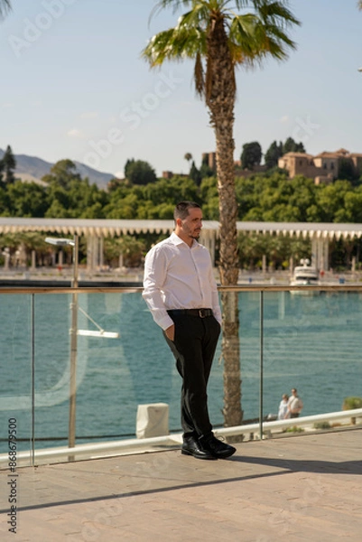 Fototapeta Hombre joven con traje y camisa en sitio lujoso con mar.  Business man. Trabajando con tablet y móvil. 