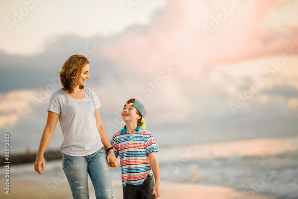 Fototapeta Young happy beautiful mother and her son having fun on the beach