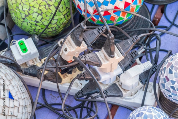 Fototapeta Old and damaged electric adapter power plug has many appliances are plugged outlet socket concept of risk danger overloaded current electrical. Overloaded power plugs, close up