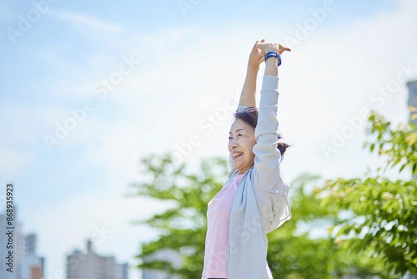 Fototapeta 春の新緑の中ストレッチをを行うスポーツウェアをきたシニア女性