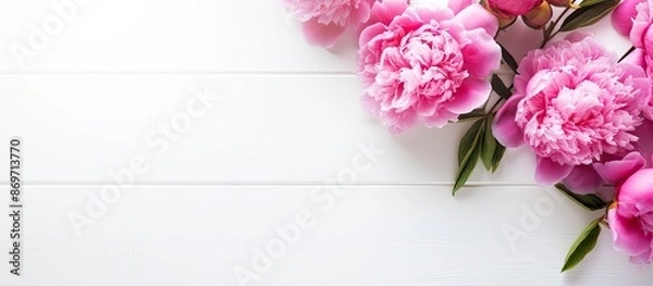 Fototapeta Top view of a feminine workspace with a close-up image of bright pink peonies against a white background, perfect for freelancing and creative endeavors, featuring ample copy space.