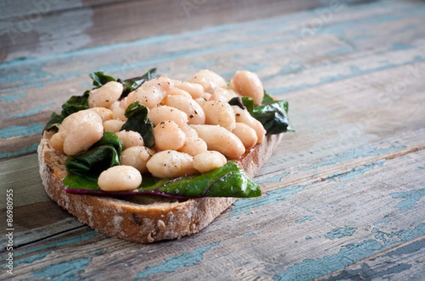 Obraz White cannellini beans, spinach and garlic on sourdough bread. A healthy vegetarian snack served on a rustic wood table.