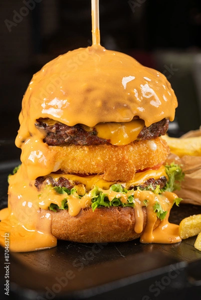 Obraz A large burger is topped with melted cheddar cheese.