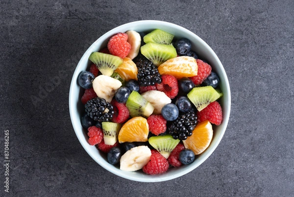 Fototapeta Fruit salad in a blue bowl on black slate background. Top view