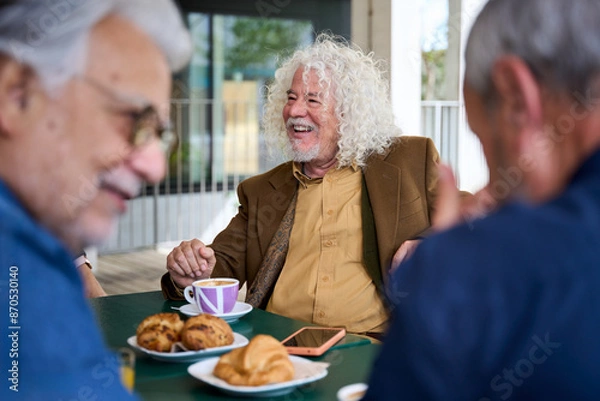 Obraz Mature grey haired man smiling enjoying coffee with his group of friends on terrace of old people home. Meeting of senior Caucasian male persons sitting together having snack or breakfast outdoors