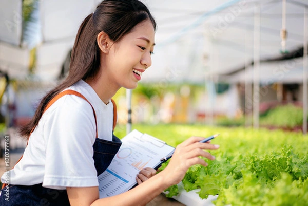 Obraz A woman is looking at a plant and writing something down in a notebook