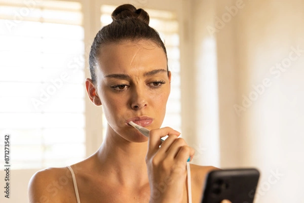 Fototapeta Brushing teeth, woman using smartphone and focusing on screen at home