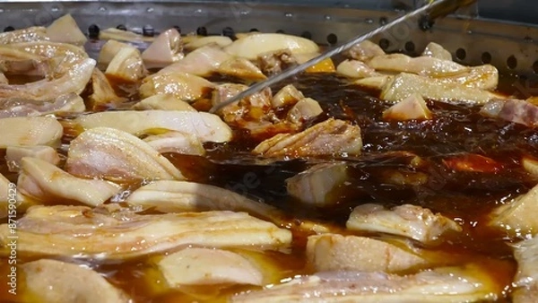 Fototapeta Pork ribs are being cooked on an industrial scale in large pans, simmering in a rich broth.