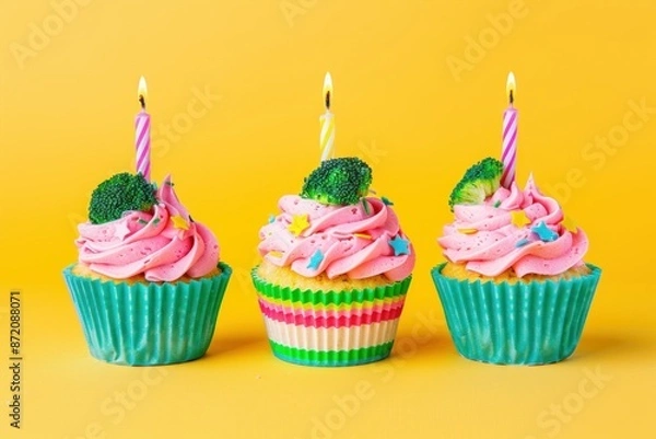 Fototapeta Celebratory cupcakes with pink frosting and candles on vibrant yellow background for festive occasions