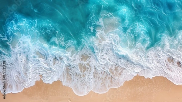 Fototapeta An aerial view of ocean waves gently washing over a sandy shore, showing the beauty of the coastline and the seamless blend of water and land in a serene, natural setting.