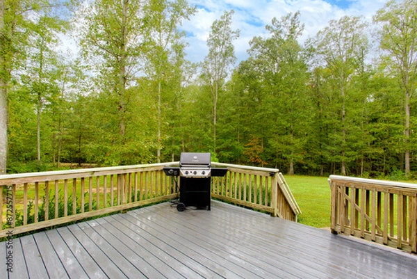 Fototapeta Wooden Deck With Barbecue Grill Set Against A Spacious, Lush, Green Backyard
