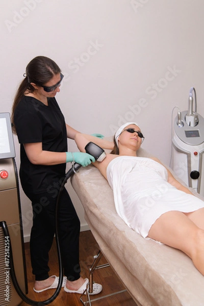 Obraz A professional performing laser hair removal on a client's armpit using a specialized device in a beauty clinic.