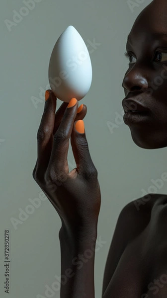 Fototapeta Portrait of a black beauty model balancing an egg shaped object on her fingertips, orange nail polish