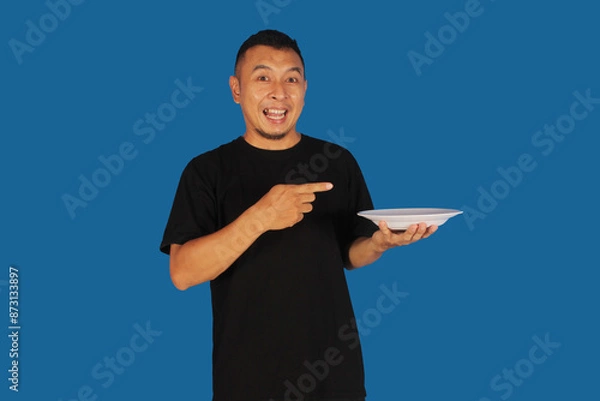 Fototapeta Attractive and confident Asian man pointing to right side of empty plate
