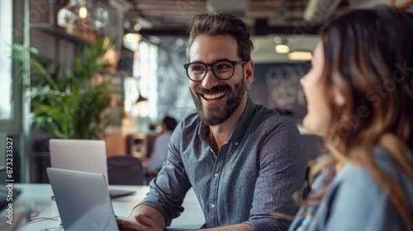 Fototapeta Smiling businessman collaborating with female colleague on laptop in open office space
