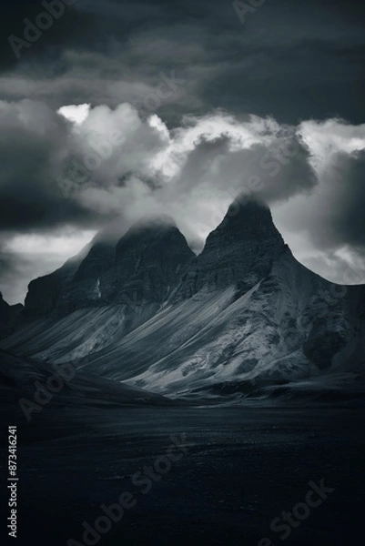 Fototapeta There are two large mountains in the distance. They are covered in snow and clouds. The sky is dark and cloudy.

