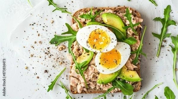 Fototapeta Healthy tuna toast with avocado, egg, and fresh arugula on whole grain bread, top-down view
