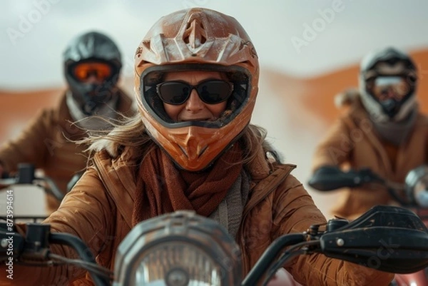 Fototapeta A group of bikers wearing helmets and scarves ride together in a desert landscape, showcasing their adventurous spirit and camaraderie in this rugged environment.