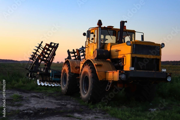 Fototapeta Cultivator on agricultural field at golden hour. Machine in field at sunset.
