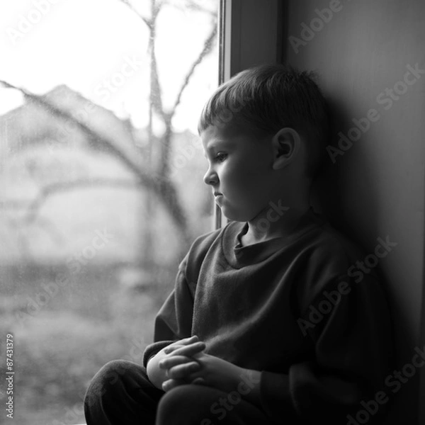 Fototapeta small boy sitting near window and thnking about something