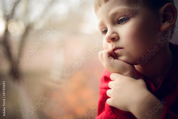 Fototapeta small boy sitting near window and thnking about something