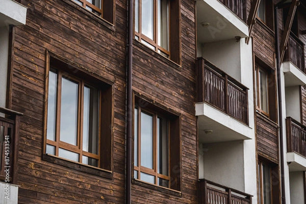 Fototapeta A beautiful wooden facade with balconies and windows that shine in the light of the setting sun