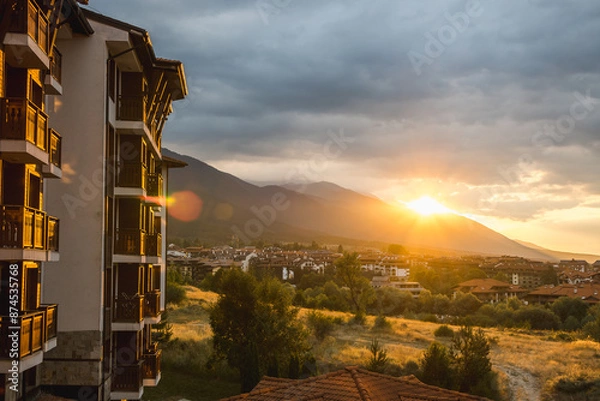 Fototapeta View of Bansko and the surrounding mountains as the setting sun breaks through the clouds, Bulgaria