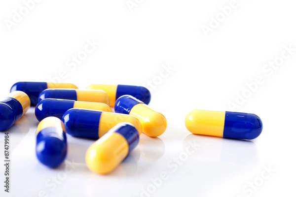 Fototapeta Tablets blue and yellow  scattered capsules shot front on on a white background