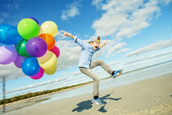 Fototapeta Happy boy plays with colored balloons on the beach