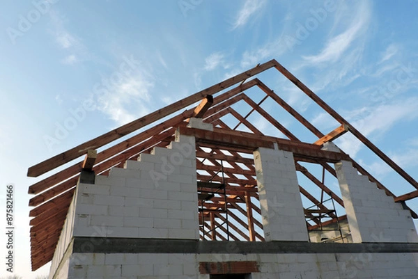 Fototapeta An "A" frame timber roof truss in a house under construction seen from the bottom, walls made of aac blocks, a rough window opening, a reinforced brick lintel, a scaffolding