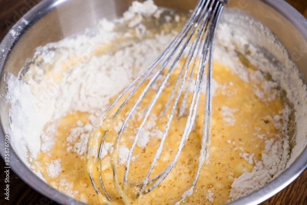 Fototapeta Bowl of batter and whisk on wooden table. Close-up of mixing dough for bakery and cooking. Ingredients for waffles, cakes or pancakes. Dough preparation process