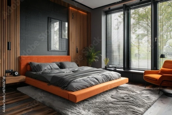 Fototapeta Contemporary minimalist bedroom showcasing a coral bed, gray walls, and wooden flooring, complemented by a black screen on the left wall, window blinds, and an orange armchair