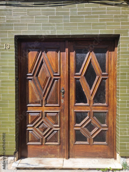 Fototapeta Intricate wooden double doors with geometric patterns on a green tiled wall