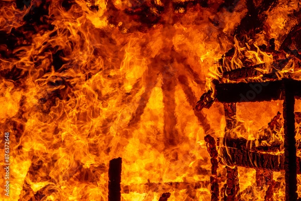 Fototapeta A dramatic image of a fierce fire burning intensely against the dark night sky. The bright orange and yellow flames highlight the raw energy and destructive power of the blaze. Copy space available.
