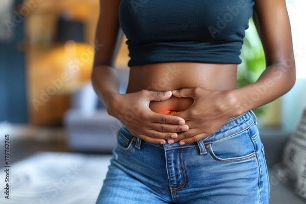 Obraz Close-up of a woman touching her stomach, indicating abdominal pain or digestive issues. Indoor shot with casual clothing.