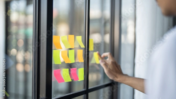 Fototapeta Man organizing project tasks Colorful sticky notes on glass of meeting room