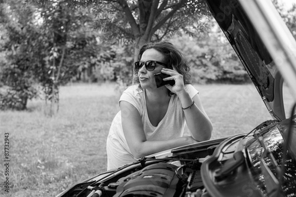 Fototapeta Young attractive girl with a broken car. Young girl with sunglasses, leaning on the car that broke down. She is calling for road assistance. 

